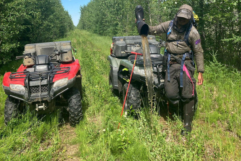 A field tech empties his boot beside 2 ATVs